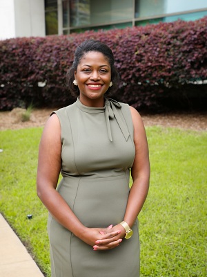 Dr Keisha Ray, olive green dress standing in front of green grass and purple shrubbery